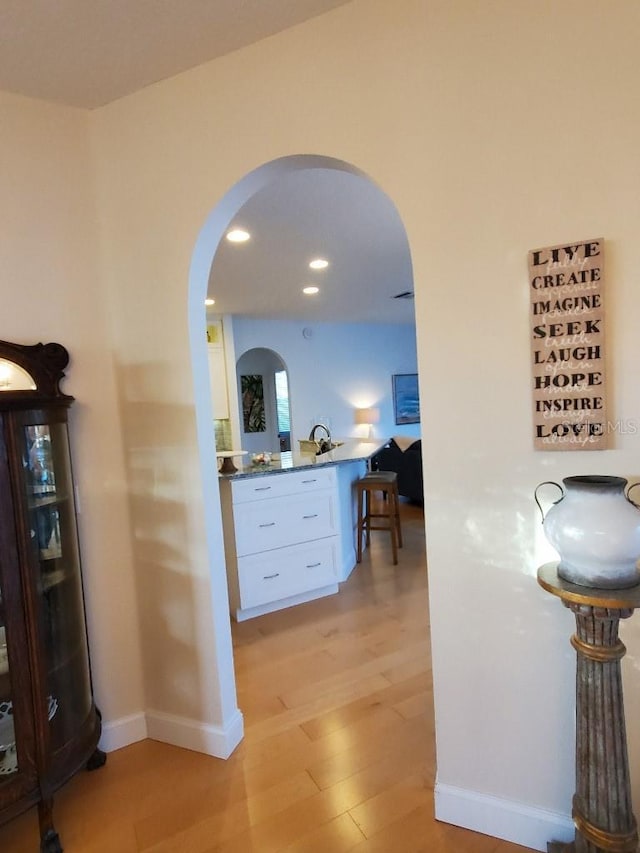 corridor with arched walkways, baseboards, light wood finished floors, and recessed lighting