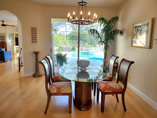 dining area featuring light wood-style floors, baseboards, arched walkways, and ceiling fan with notable chandelier