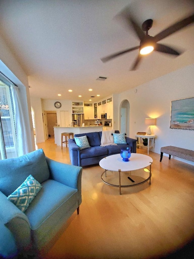 living area featuring arched walkways, recessed lighting, a ceiling fan, visible vents, and light wood finished floors