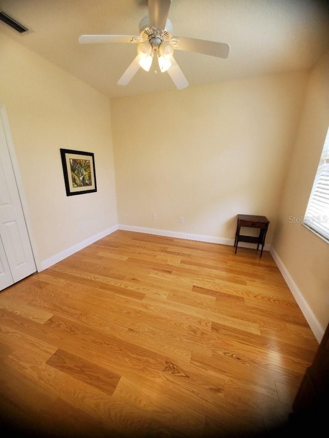 unfurnished room with a ceiling fan, light wood-type flooring, visible vents, and baseboards