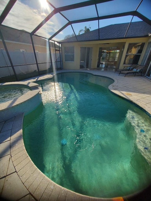 view of pool with a patio area, a pool with connected hot tub, fence, and glass enclosure