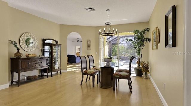 dining space with light wood finished floors, visible vents, baseboards, ceiling fan with notable chandelier, and arched walkways