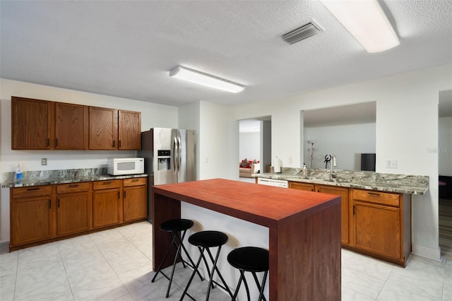 kitchen with sink, white appliances, a breakfast bar, dark stone countertops, and kitchen peninsula