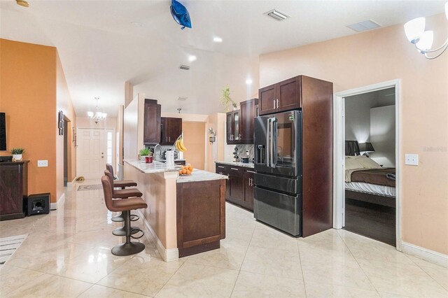 kitchen with high quality fridge, lofted ceiling, a kitchen breakfast bar, dark brown cabinets, and an inviting chandelier