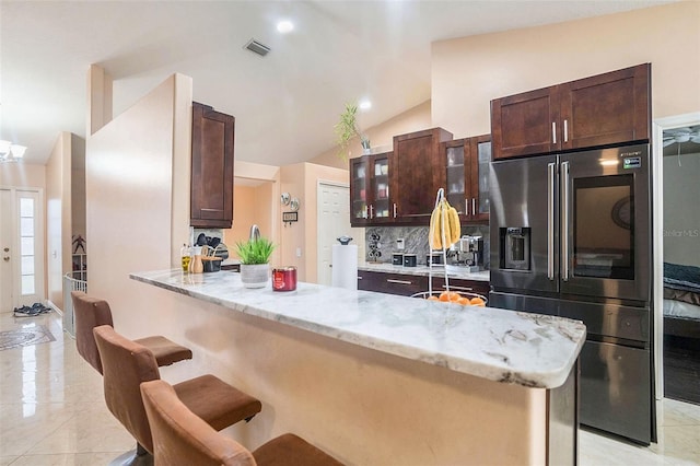 kitchen featuring stainless steel refrigerator with ice dispenser, a kitchen bar, kitchen peninsula, light stone countertops, and decorative backsplash