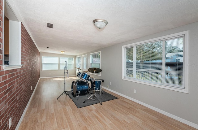 exercise area featuring brick wall, a textured ceiling, and light hardwood / wood-style floors