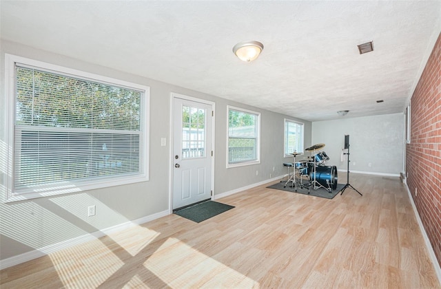 exercise room with brick wall, a textured ceiling, and light hardwood / wood-style flooring