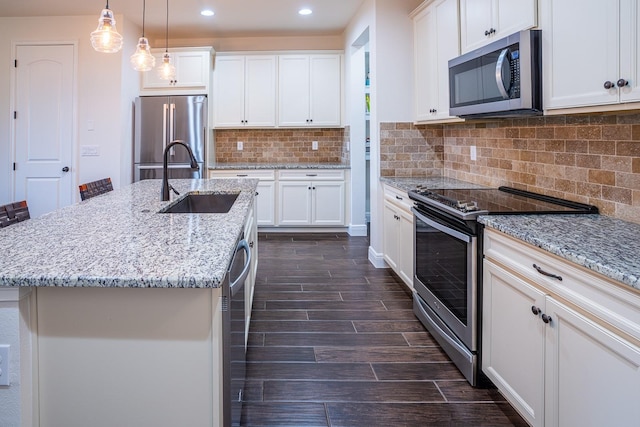 kitchen with appliances with stainless steel finishes, a center island with sink, white cabinets, and decorative light fixtures