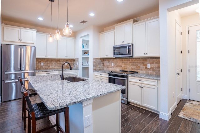 kitchen with sink, appliances with stainless steel finishes, a kitchen island with sink, white cabinetry, and a kitchen bar