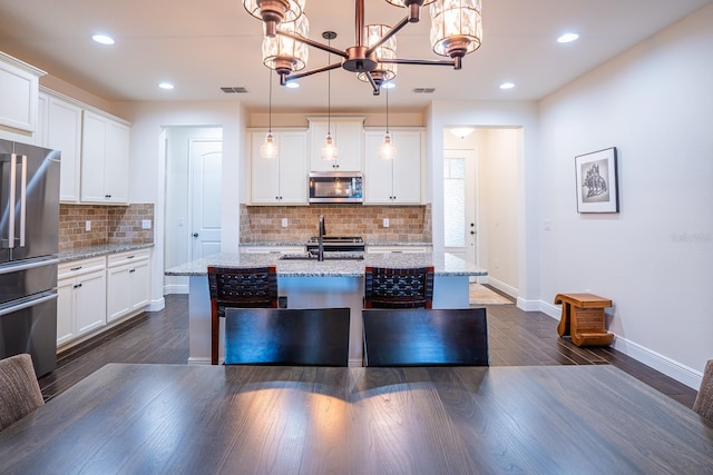 kitchen featuring stainless steel appliances, decorative light fixtures, light stone countertops, and white cabinets