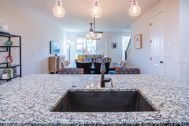 kitchen with an inviting chandelier, sink, light stone countertops, and hanging light fixtures