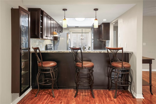 bar featuring dark wood-type flooring, light stone counters, hanging light fixtures, stainless steel refrigerator, and backsplash