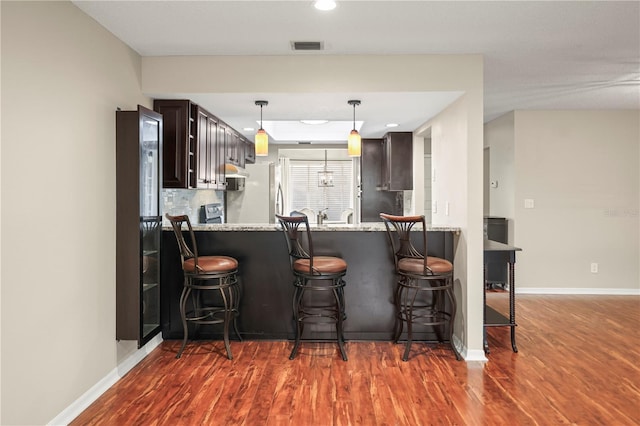 kitchen featuring dark wood-type flooring, light stone countertops, a breakfast bar, and dark brown cabinets