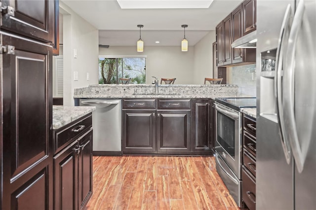 kitchen with sink, light hardwood / wood-style flooring, hanging light fixtures, stainless steel appliances, and light stone counters