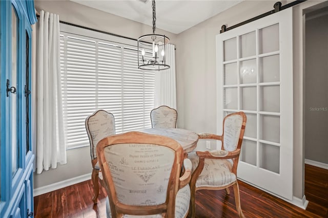 dining area featuring dark wood-type flooring, a barn door, and a notable chandelier