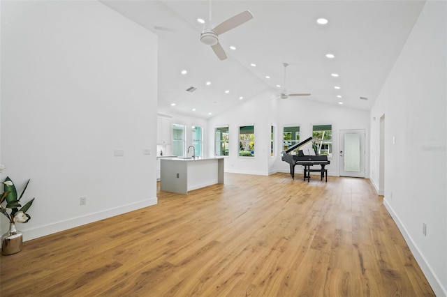 unfurnished living room with ceiling fan, sink, high vaulted ceiling, and light hardwood / wood-style flooring