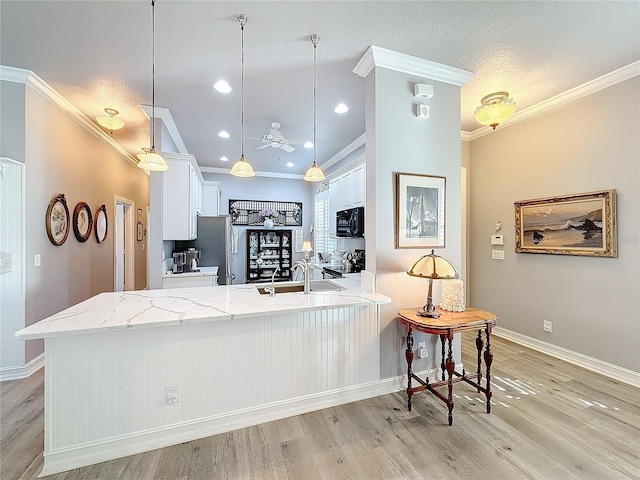 kitchen with pendant lighting, white cabinets, light stone counters, stainless steel appliances, and light hardwood / wood-style flooring