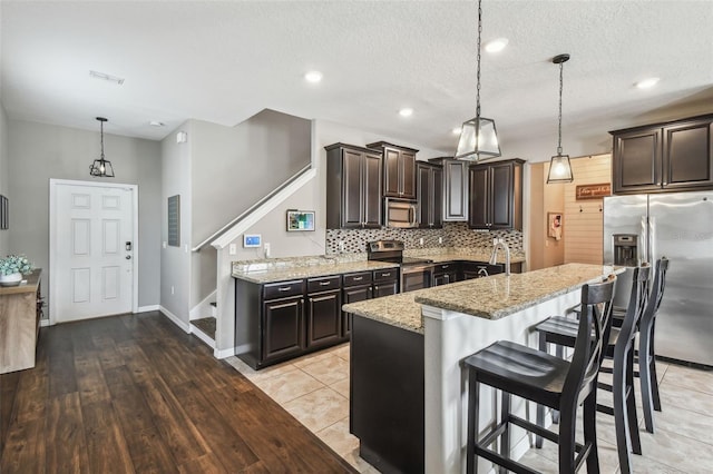 kitchen with stainless steel appliances, an island with sink, a breakfast bar, and pendant lighting