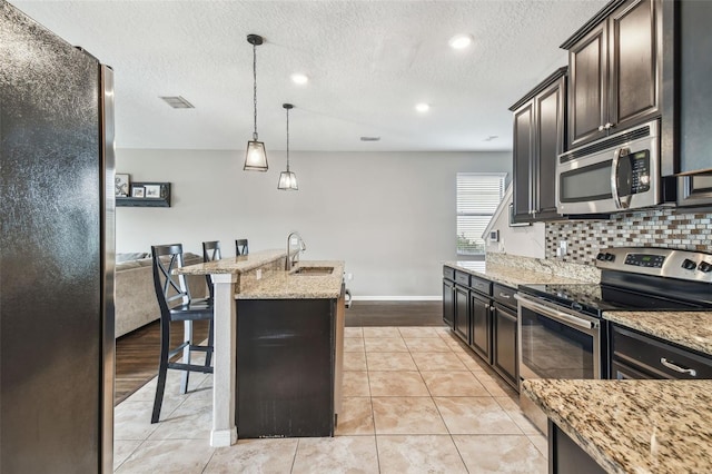 kitchen with sink, a breakfast bar area, hanging light fixtures, appliances with stainless steel finishes, and an island with sink