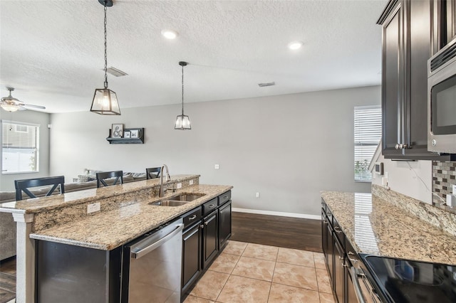 kitchen with pendant lighting, sink, light tile patterned floors, stainless steel appliances, and a center island with sink