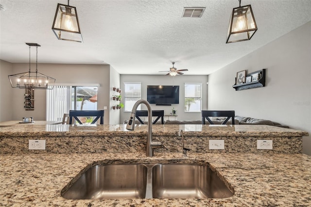 kitchen with pendant lighting, ceiling fan, sink, and stone counters