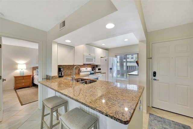 kitchen with light stone counters, white appliances, kitchen peninsula, and white cabinets