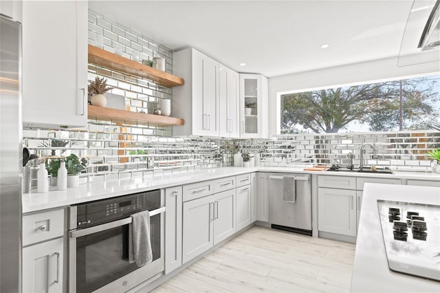 kitchen featuring appliances with stainless steel finishes, white cabinetry, sink, backsplash, and light hardwood / wood-style floors