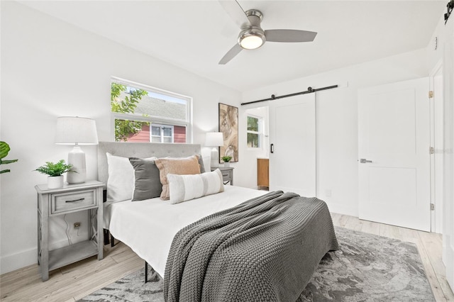 bedroom featuring ceiling fan, a barn door, and light wood-type flooring