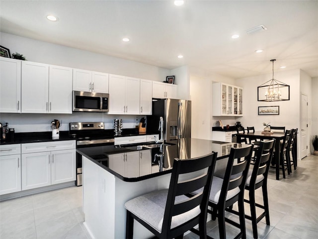 kitchen featuring dark countertops, an island with sink, a breakfast bar, stainless steel appliances, and white cabinetry