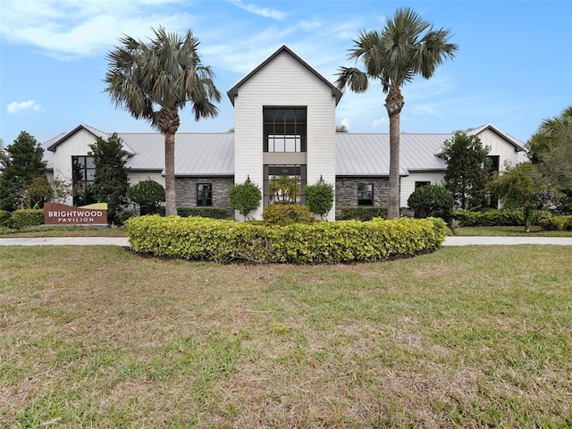 view of front of property featuring metal roof, stone siding, a front lawn, and a standing seam roof