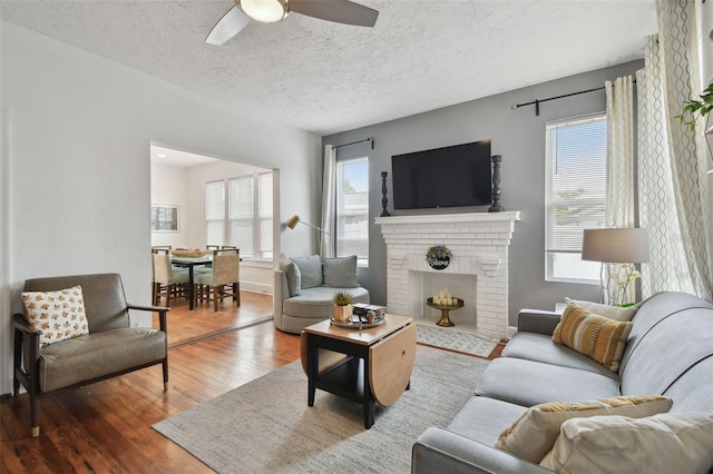 living room featuring hardwood / wood-style flooring, ceiling fan, a brick fireplace, and a textured ceiling