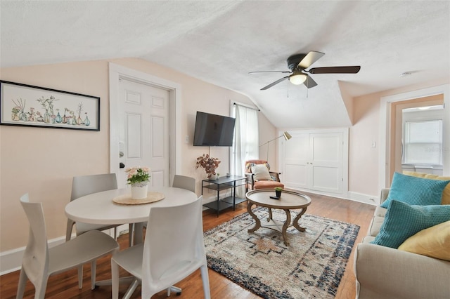 living room featuring vaulted ceiling, wood-type flooring, ceiling fan, and a textured ceiling