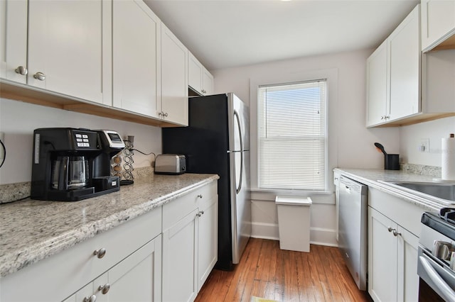 kitchen with white cabinetry, appliances with stainless steel finishes, light stone counters, and light hardwood / wood-style flooring