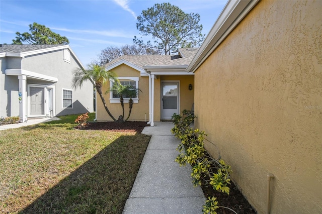 property entrance featuring stucco siding, a shingled roof, and a yard