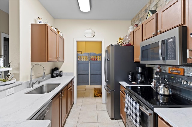 kitchen with appliances with stainless steel finishes, light tile patterned flooring, a sink, and light stone countertops