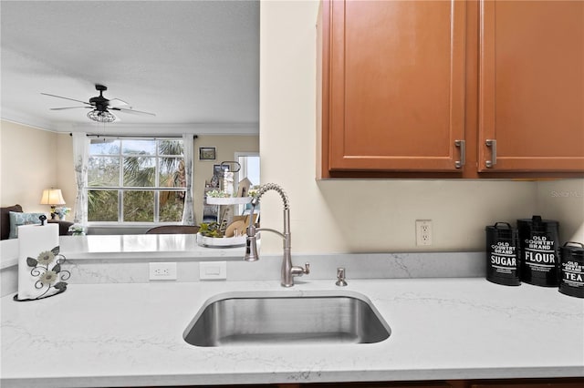 kitchen with ceiling fan, ornamental molding, a sink, and light stone counters