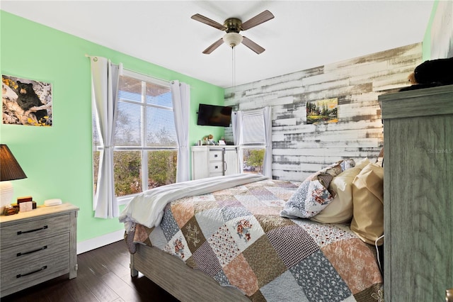 bedroom with an accent wall, dark wood finished floors, a ceiling fan, and baseboards