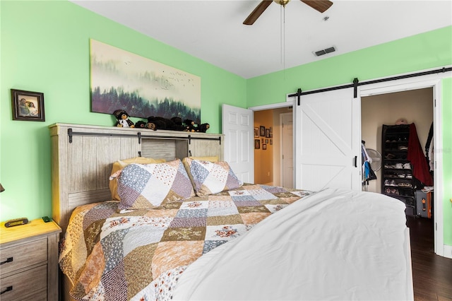 bedroom featuring wood finished floors, visible vents, ceiling fan, and a barn door