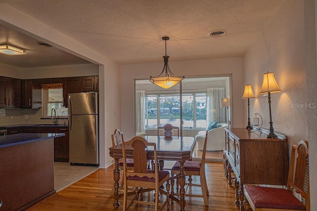 dining room with sink, a textured ceiling, and light wood-type flooring