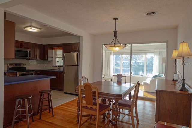 dining area featuring sink, light hardwood / wood-style floors, and a textured ceiling