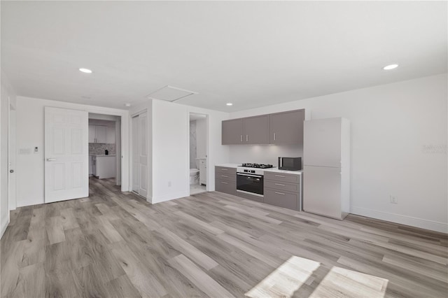 kitchen featuring gray cabinetry, stainless steel oven, and light wood-type flooring