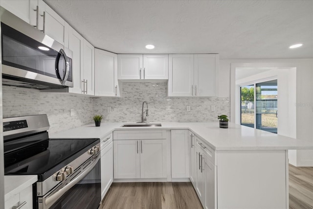 kitchen with sink, white cabinetry, light hardwood / wood-style flooring, kitchen peninsula, and stainless steel appliances