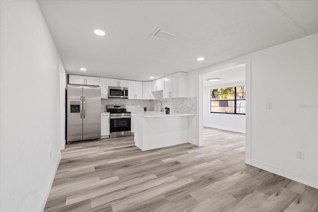 kitchen with tasteful backsplash, light hardwood / wood-style flooring, kitchen peninsula, stainless steel appliances, and white cabinets