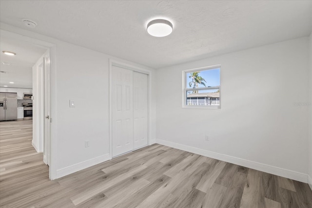 unfurnished bedroom with light hardwood / wood-style flooring, stainless steel fridge, a closet, and a textured ceiling