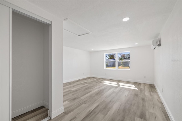 spare room featuring light hardwood / wood-style floors, a textured ceiling, and an AC wall unit