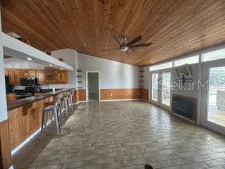 unfurnished living room featuring wood walls, lofted ceiling, ceiling fan, wood ceiling, and french doors