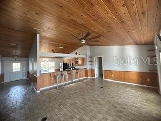 unfurnished living room with wooden walls, ceiling fan, dark hardwood / wood-style floors, and wooden ceiling