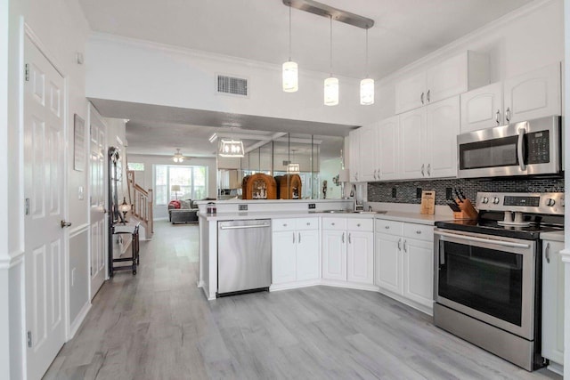 kitchen with stainless steel appliances, kitchen peninsula, hanging light fixtures, and white cabinets