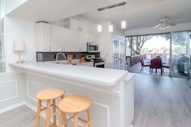 kitchen with appliances with stainless steel finishes, decorative light fixtures, white cabinets, a kitchen bar, and kitchen peninsula