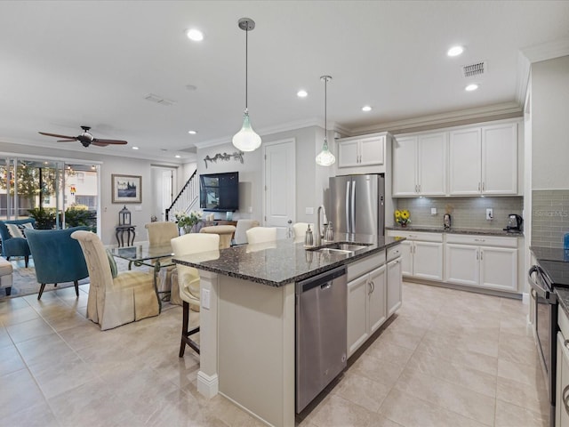 kitchen featuring dark stone countertops, sink, stainless steel appliances, and an island with sink